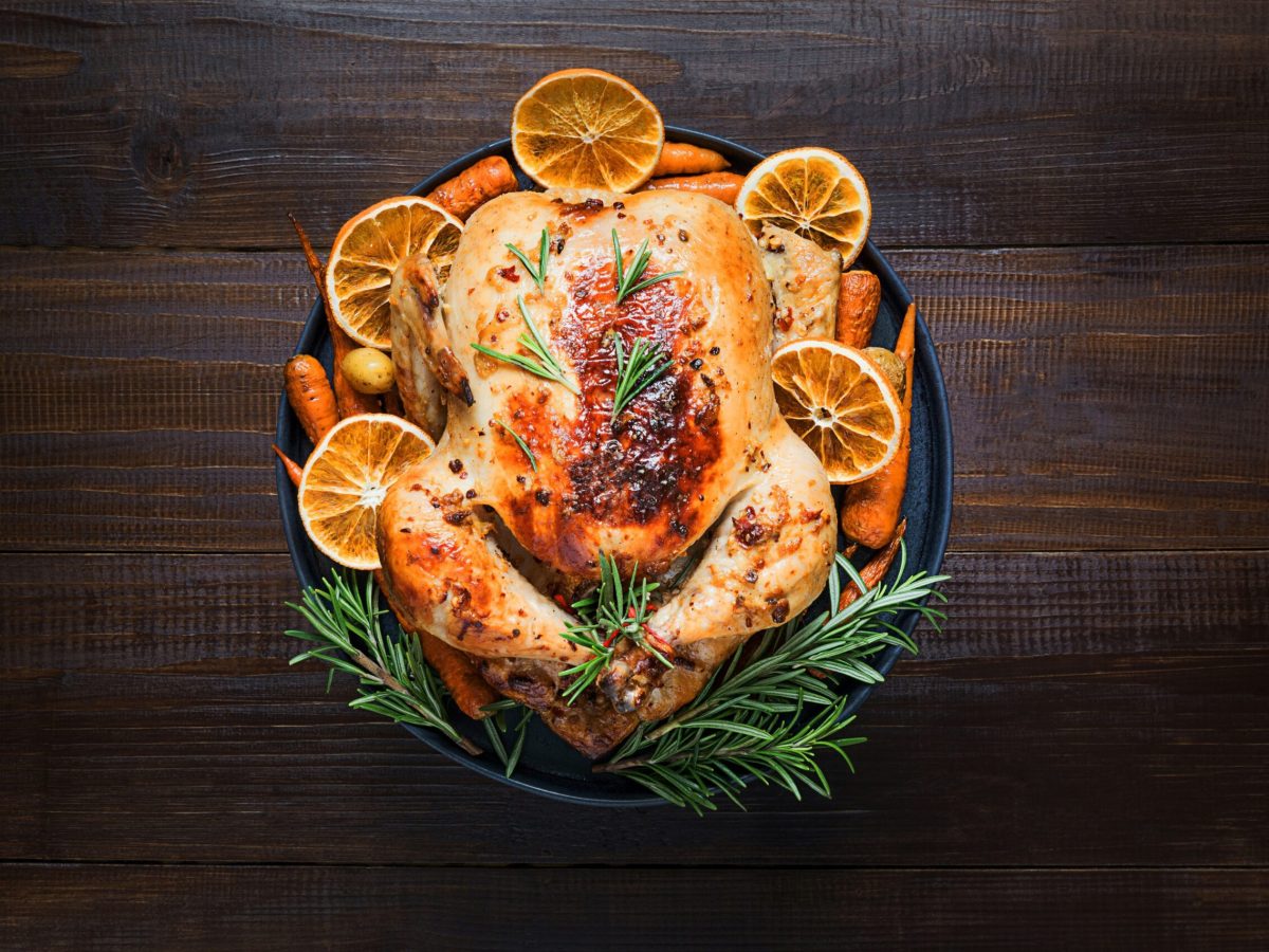 Traditional roasted turkey garnish rosemary and sliced orange on dark wooden table. Xmas dinner or Thanksgiving day. Top view. Horizontal orientation.